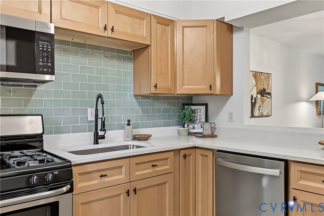 Light-toned wood cabinetry, subway tile backsplash, stainless steel appliances, solid-surface countertops, and a matte black gooseneck faucet