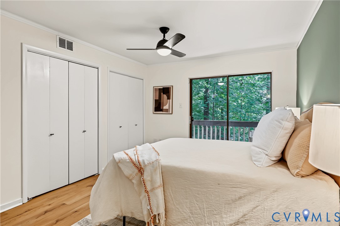 Room featuring wood-finish flooring, dual-door closets, a modern black ceiling fan, and sliding glass doors with exterior balcony access
