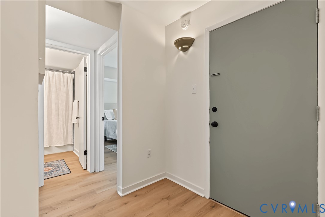 Entryway featuring wood-finish flooring, a matte grey door with black hardware, and a wall-mounted light fixture