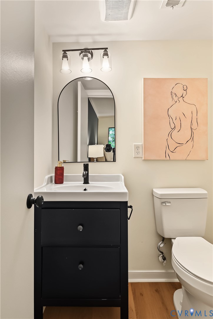 Black vanity with a white integrated basin, matte black faucet, arched wall mirror, three-light vanity fixture, and wood-finish flooring