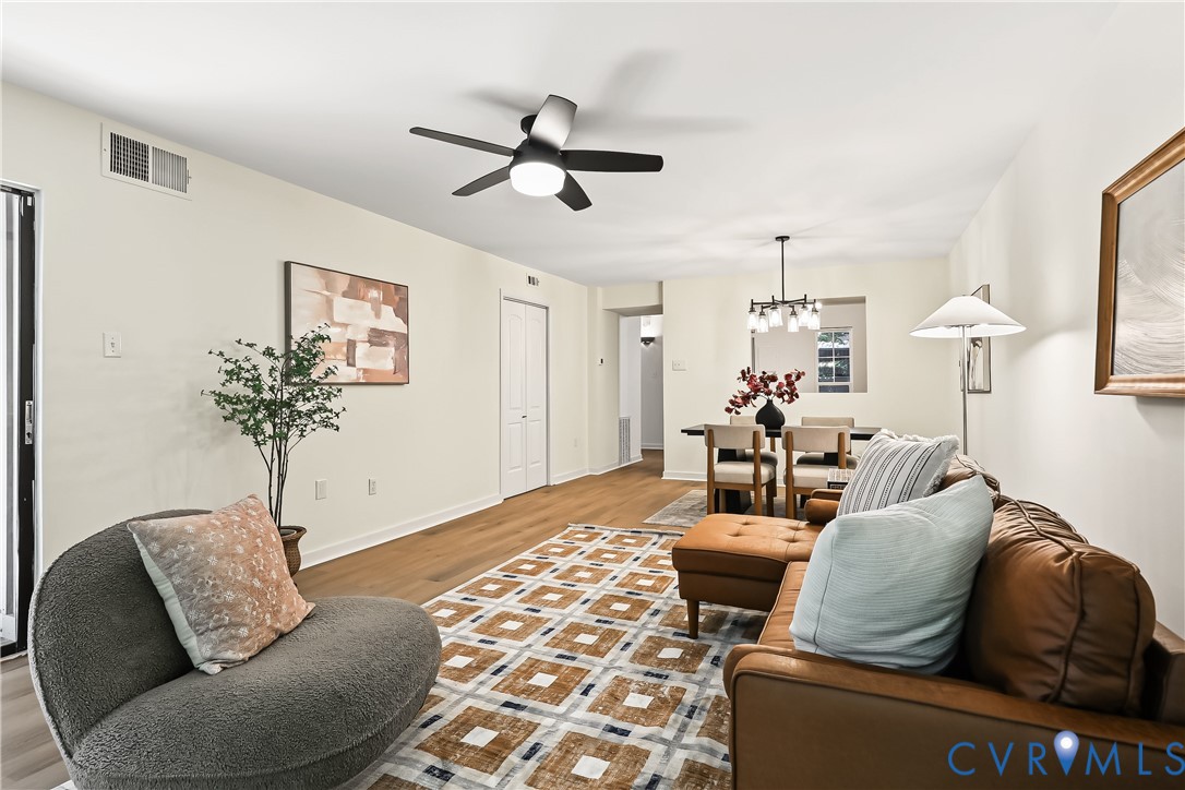 Living area featuring wood-finish flooring, a contemporary multi-blade ceiling fan with integrated lighting, and a multi-light metal chandelier