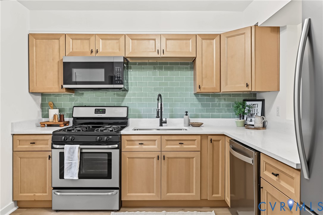 Kitchen featuring light wood cabinetry, white countertops, a sage green subway tile backsplash, a matte black gooseneck faucet, and stainless steel appliances