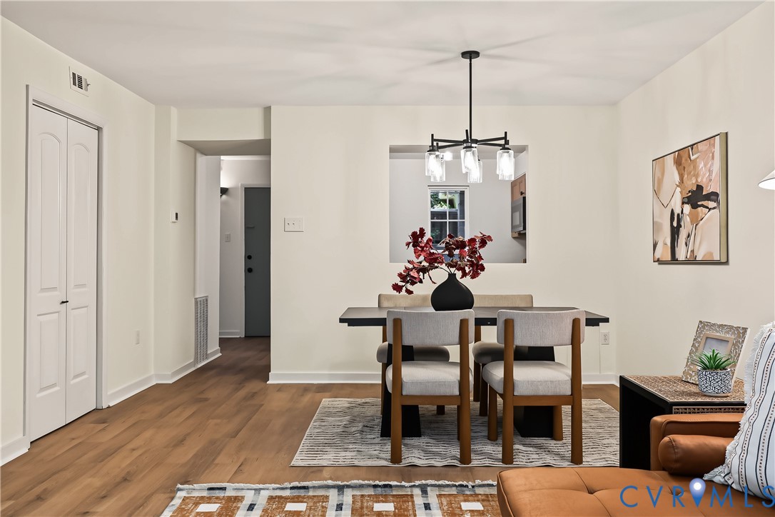 Open-concept area featuring wood-finish flooring, a matte black multi-arm chandelier with glass globe shades, and a wall cutout providing transparency to the kitchen