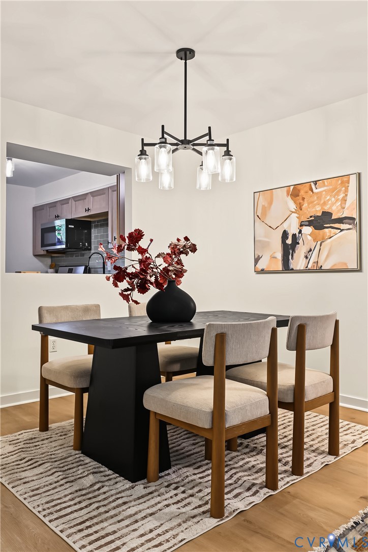 Dining space featuring wood-finish flooring, a six-light black metal chandelier with glass shades, and a structural pass-through opening