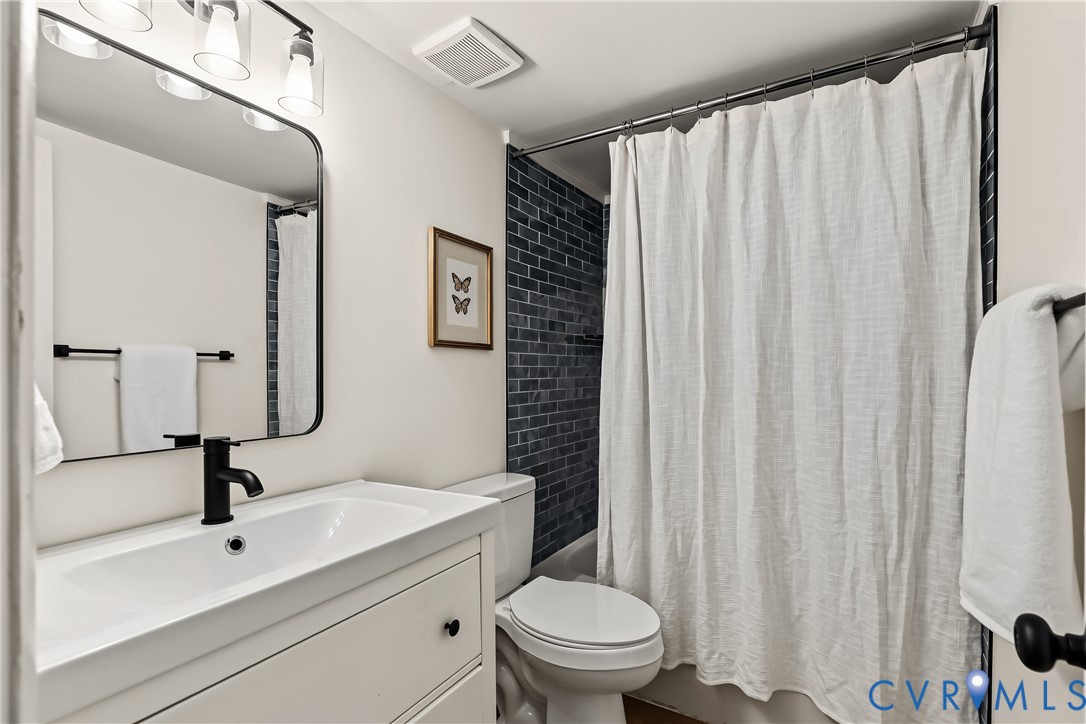Bathroom featuring a white vanity cabinet with a rectangular basin, matte black faucet, rounded rectangular mirror, and dark blue subway tile shower surround