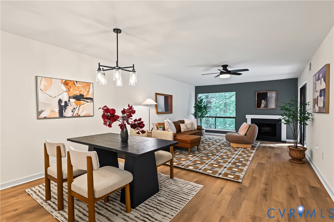 Open-concept room featuring wood-finish flooring, a matte black multi-light chandelier, a fireplace with a white mantel, and a matte black ceiling fan