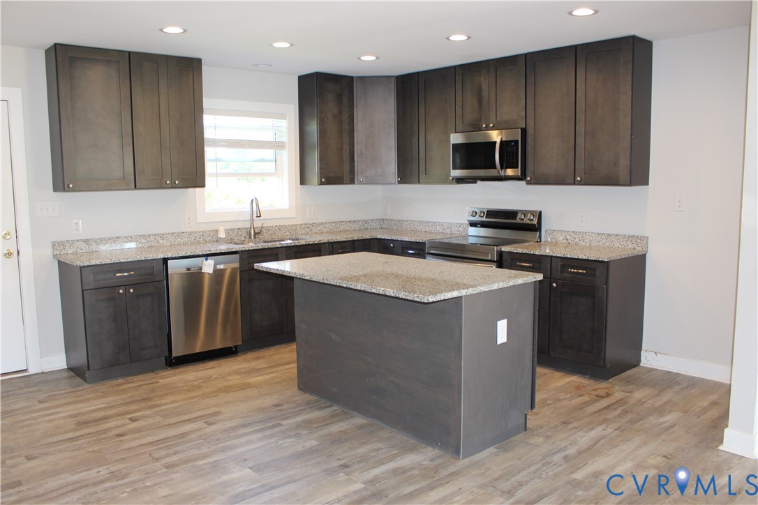 Kitchen featuring charcoal-toned cabinetry, light-toned stone-finish countertops, a central island, recessed lighting, and stainless steel appliances
