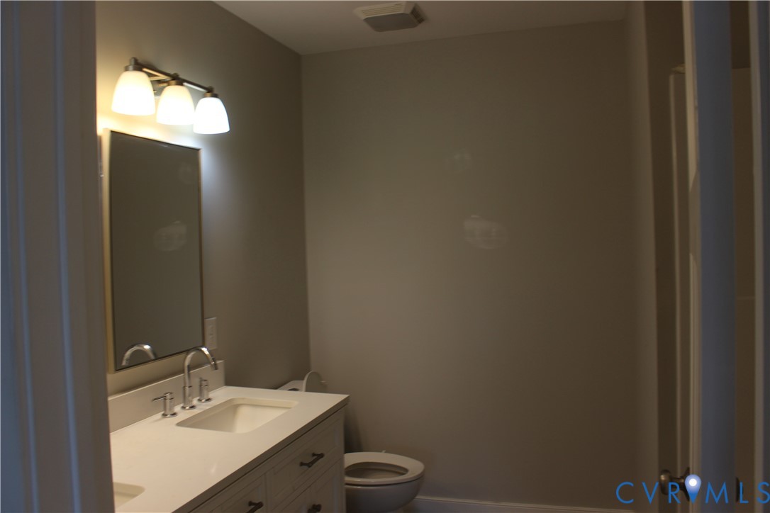 Bathroom featuring a vanity with a white countertop and integrated sink, a wall-mounted rectangular mirror, a three-light fixture, and a toilet