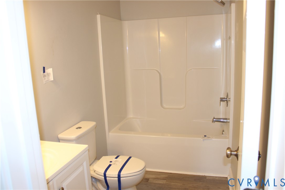 Bathroom featuring a tub and shower combination with a molded surround, a vanity, a toilet, and wood-finish flooring