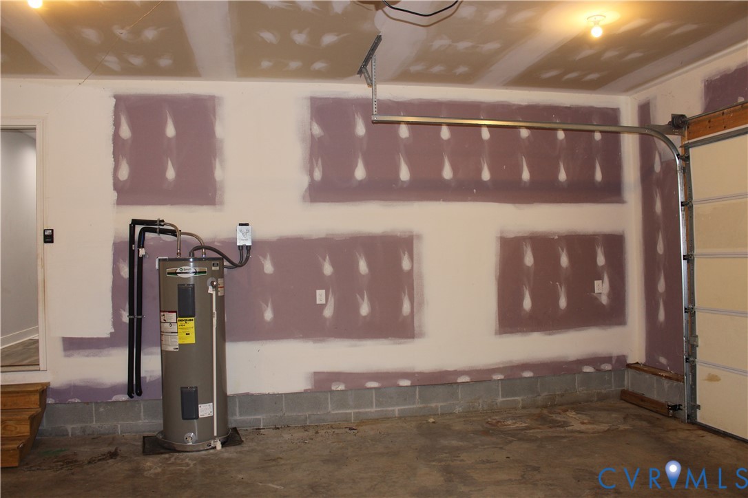 Garage interior featuring drywall panels, overhead lighting, an upright water heater, and a metal garage door system