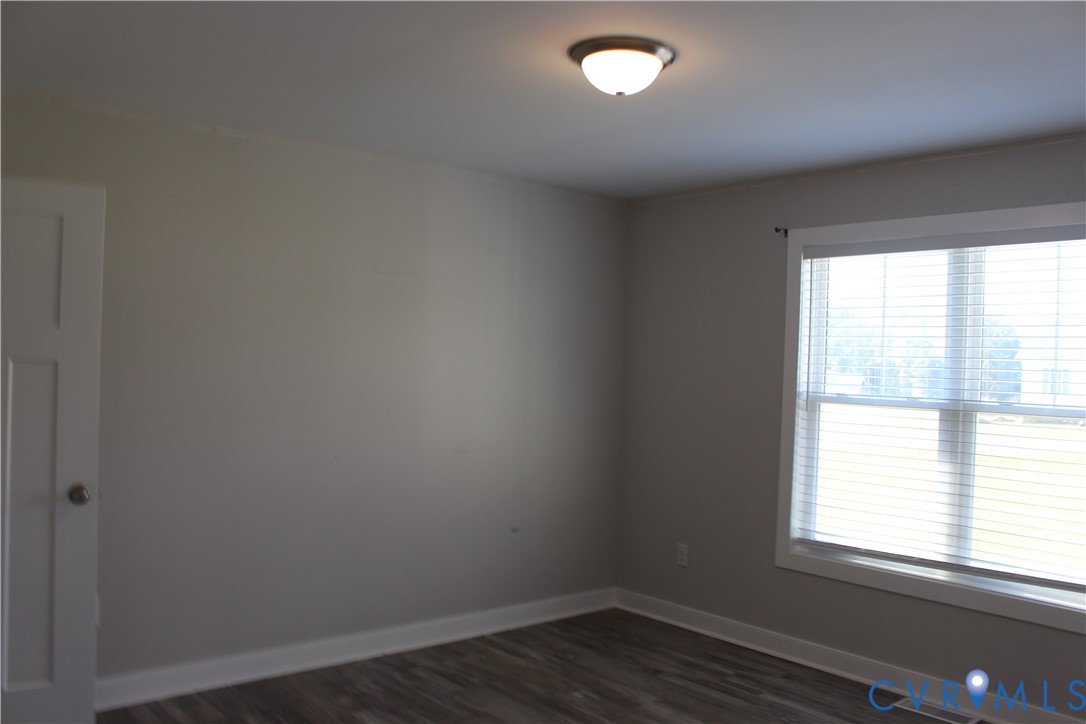 Neutral-toned interior space featuring wood-finish flooring, a flush-mount ceiling light, and a multi-pane window with interior window blinds
