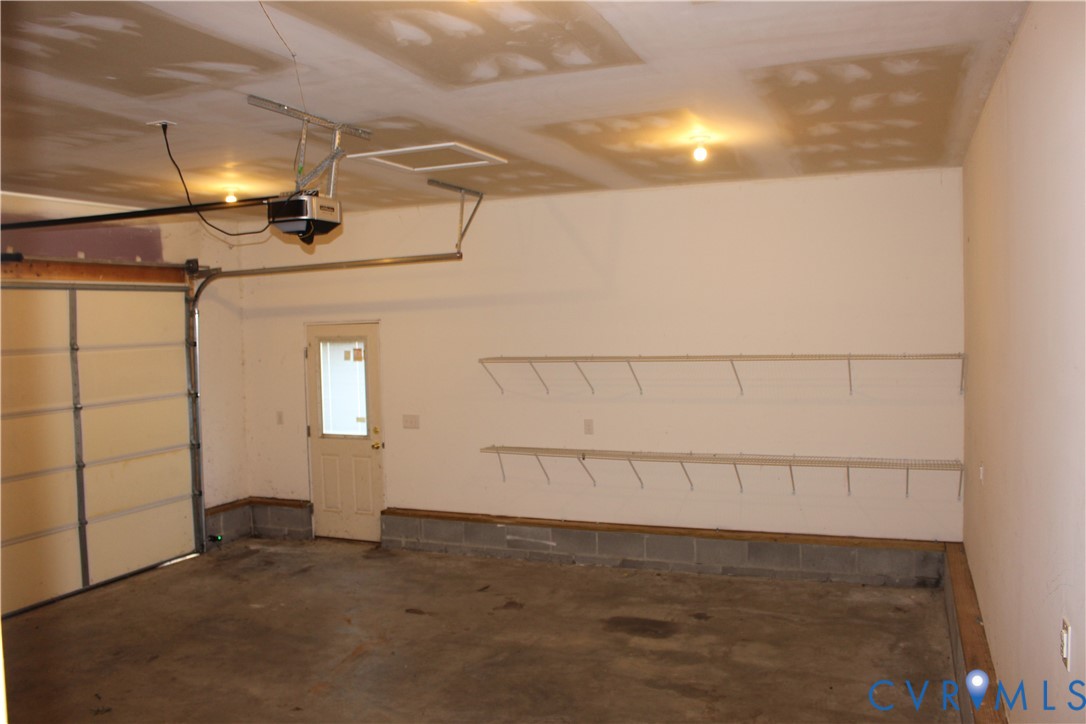 Garage space featuring a concrete floor, automated overhead door opener, exterior access door with window inset, and two levels of wall-mounted wire shelving
