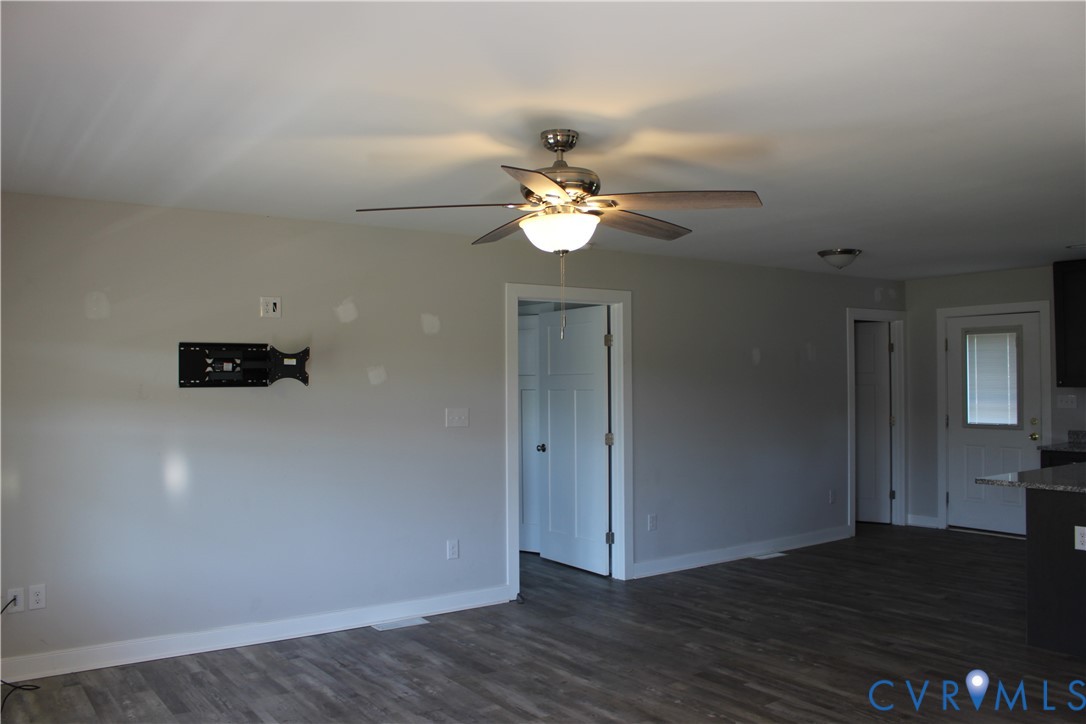 Interior featuring wood-finish flooring, a brushed metal ceiling fan with integrated lighting, neutral wall paint, and a white six-panel door