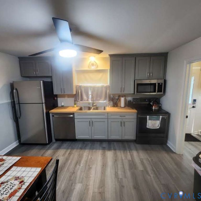 Kitchen featuring grey shaker-style cabinetry, wood-finish countertops, stainless steel appliances, dual-basin sink with pull-down faucet, and wood-finish flooring