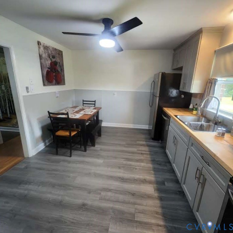 Kitchen featuring grey cabinetry, wood-finish flooring, wood-toned countertops, a stainless steel double-basin sink, and a ceiling-mounted fan with integrated lighting