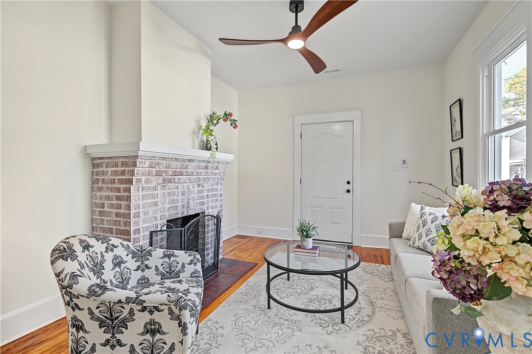 Living area featuring a brick fireplace with a mantle, wood-finish flooring, and a modern ceiling fan with integrated lighting