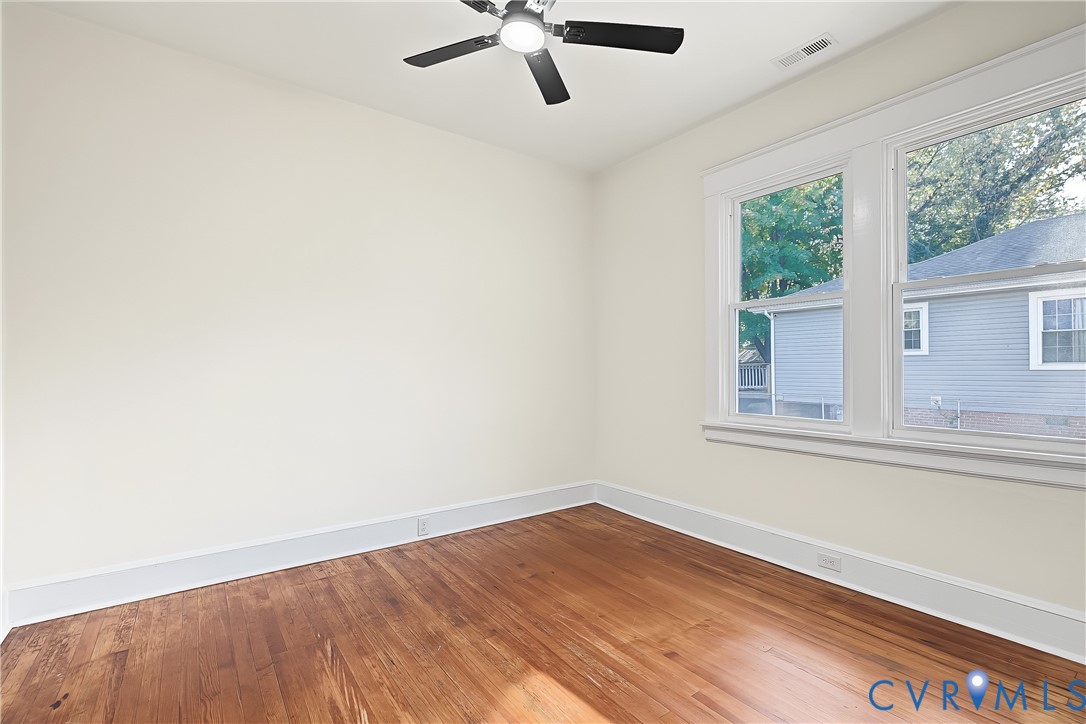 Room featuring wood-finish flooring, multi-pane windows with casing, and a ceiling-mounted fan with integrated lighting