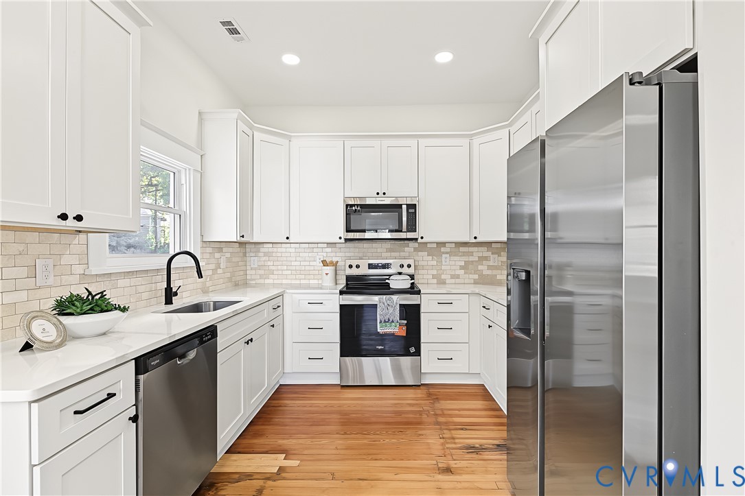 Kitchen featuring shaker-style white cabinetry, quartz countertops, subway tile backsplash, wood-finish flooring, and stainless steel appliances