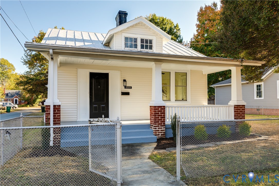 Single-story exterior featuring a metal roof, front porch with brick column bases, light-toned horizontal siding, and a centered dormer Single-story exterior featuring a metal roof, front porch with brick column bases, light-toned horizontal siding, and a centered dormer