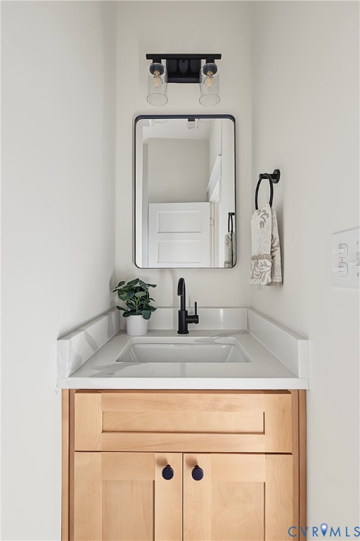 Light-wood finish vanity featuring a solid surface countertop with an integrated basin, matte black faucet, rectangular mirror, and dual-bulb industrial-style wall sconce