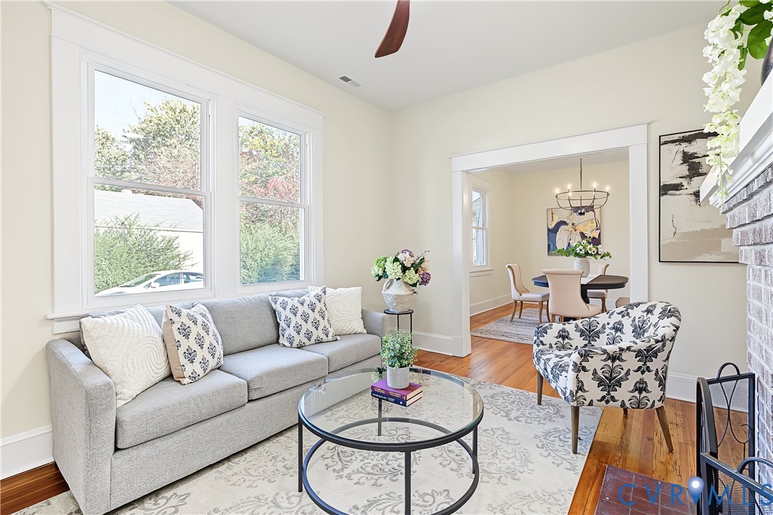 Living area featuring wood-finish flooring, tall windows with wide trim, and a brick fireplace surround