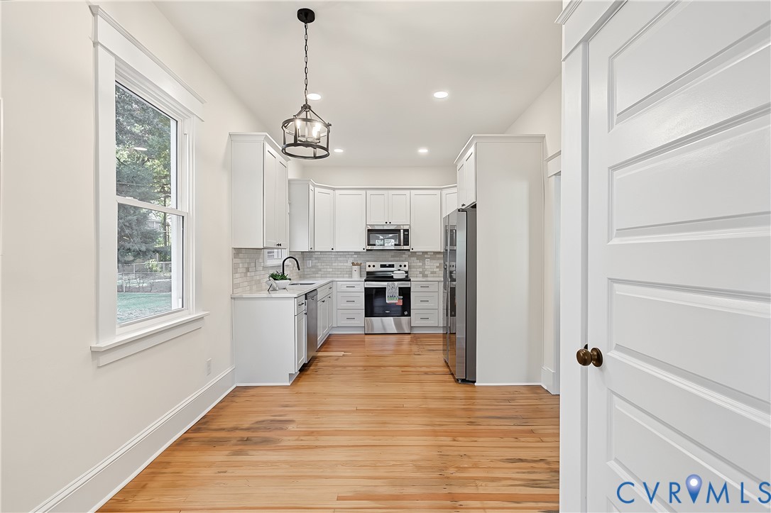 Kitchen featuring white shaker-style cabinetry, wood-finish flooring, stainless steel appliances, tiled backsplash, and decorative pendant lighting