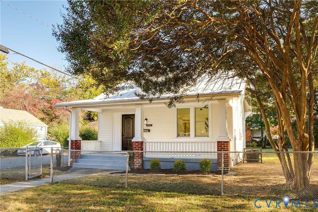 Exterior featuring white siding, a covered front porch with brick column bases, square support columns, and a metal roof