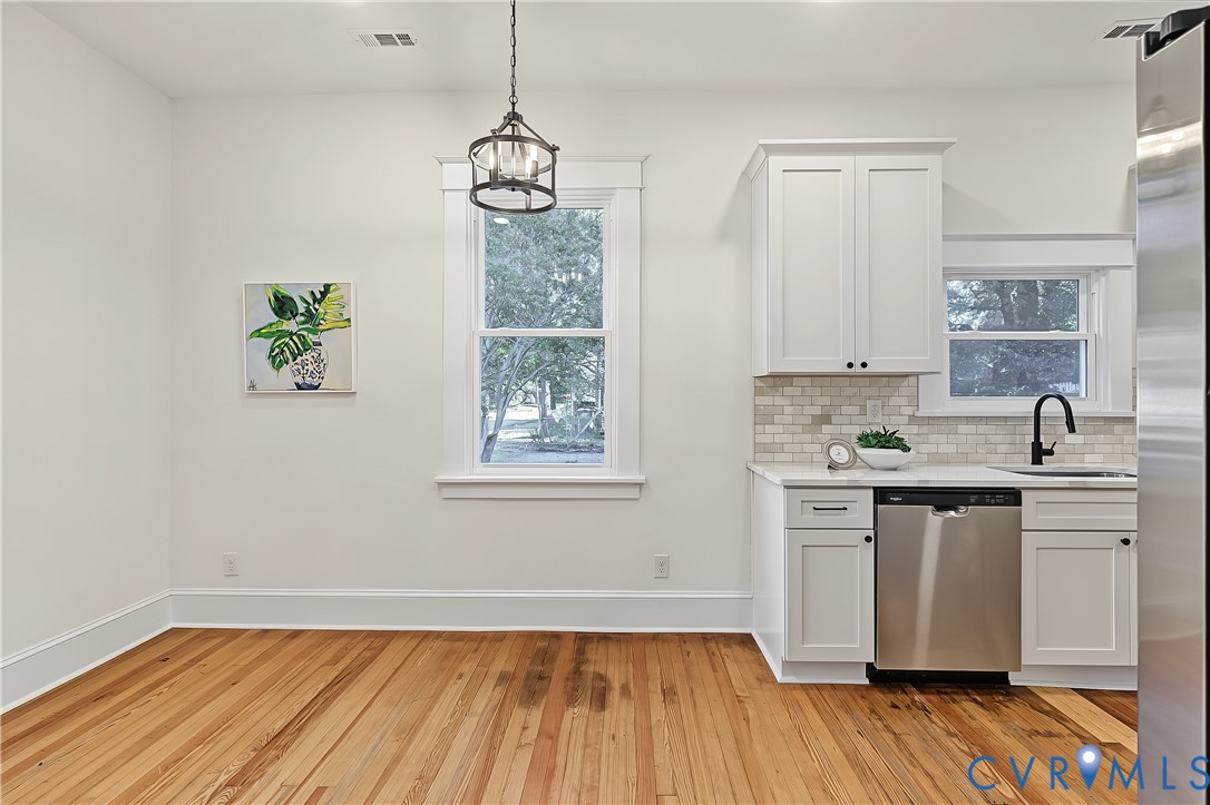 Kitchen area featuring wood-finish flooring, white shaker-style cabinetry, a brick-pattern tile backsplash, stainless steel dishwasher, and a matte black faucet