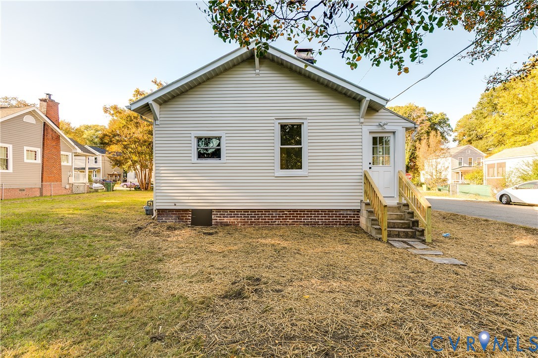 Exterior side elevation featuring horizontal vinyl siding, a brick foundation, a chimney, and a wooden staircase leading to a glass-panel entry door