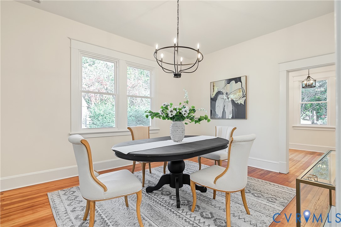 Dining area featuring wood-finish flooring, a matte black circular chandelier, and natural light provided by dual-pane windows with thick casing trim