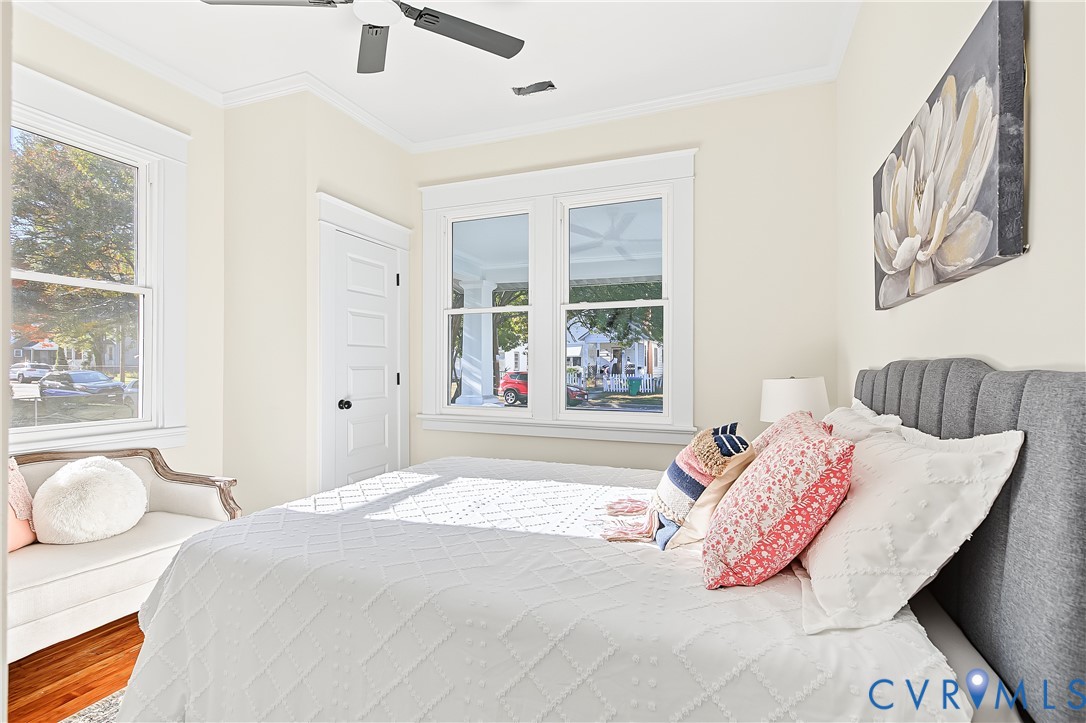 Bright room featuring wood-finish flooring, double-hung windows with substantial millwork trim, a four-panel interior door, and a ceiling-mounted fan