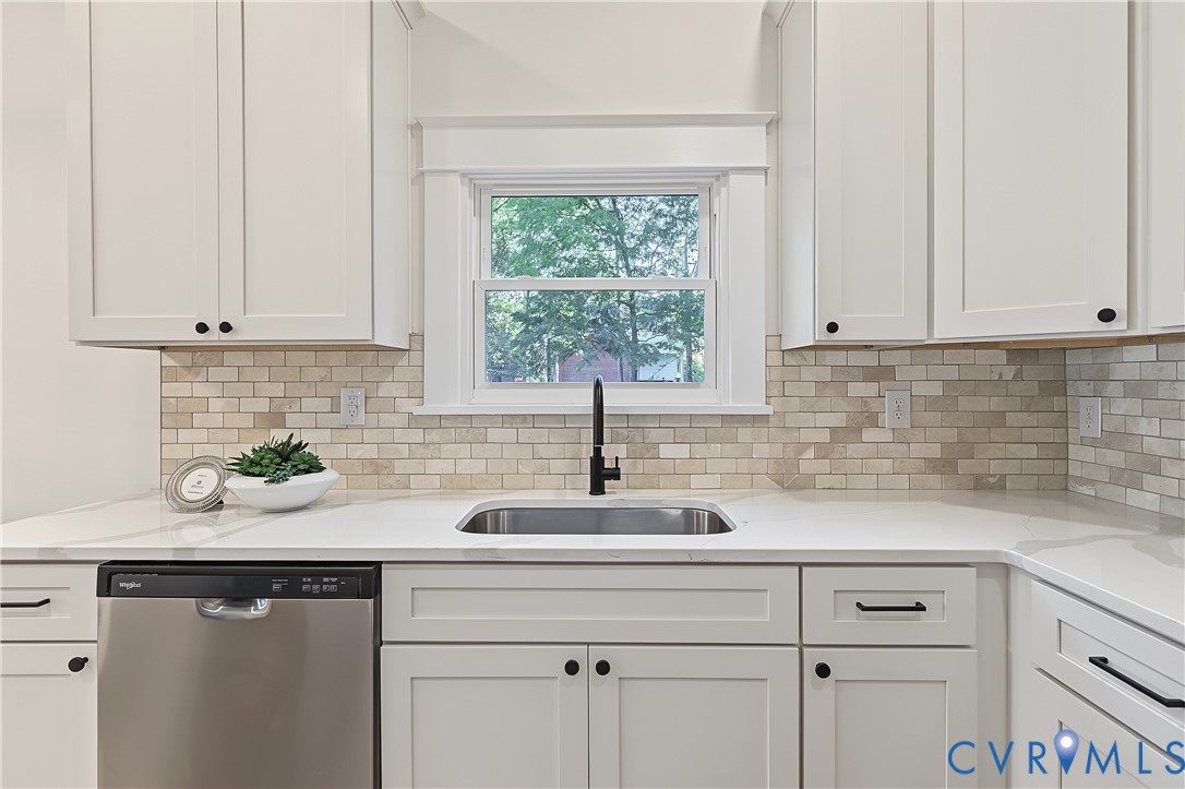 Kitchen featuring white shaker-style cabinetry, light-toned brick-patterned backsplash, stainless steel dishwasher, solid-surface countertop, and matte black plumbing fixtures