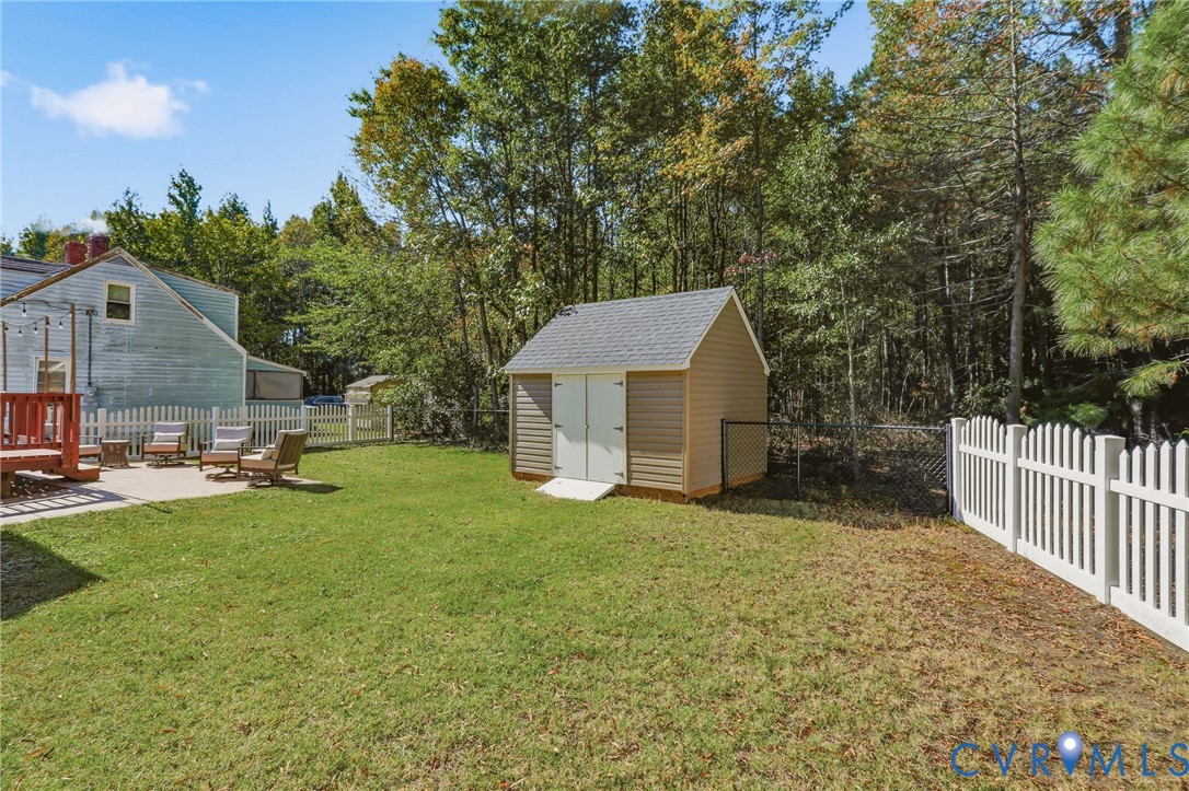 Backyard featuring a concrete stamped patio, detached storage shed with a shingled roof, white picket fencing, and a perimeter chain-link fence