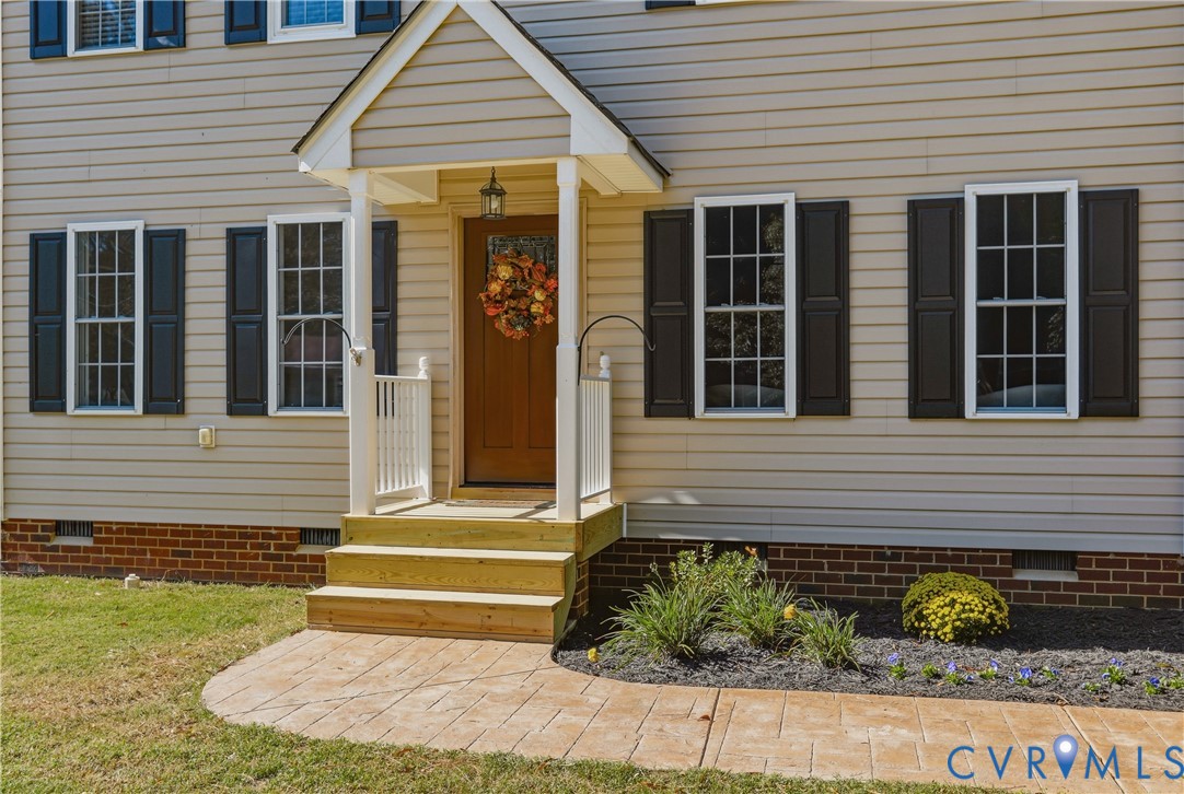 Exterior entrance featuring horizontal siding, dark decorative shutters, a covered entryway porch and a stamped concrete walkway Exterior entrance featuring horizontal siding, dark decorative shutters, a covered entryway porch and a stamped concrete walkway