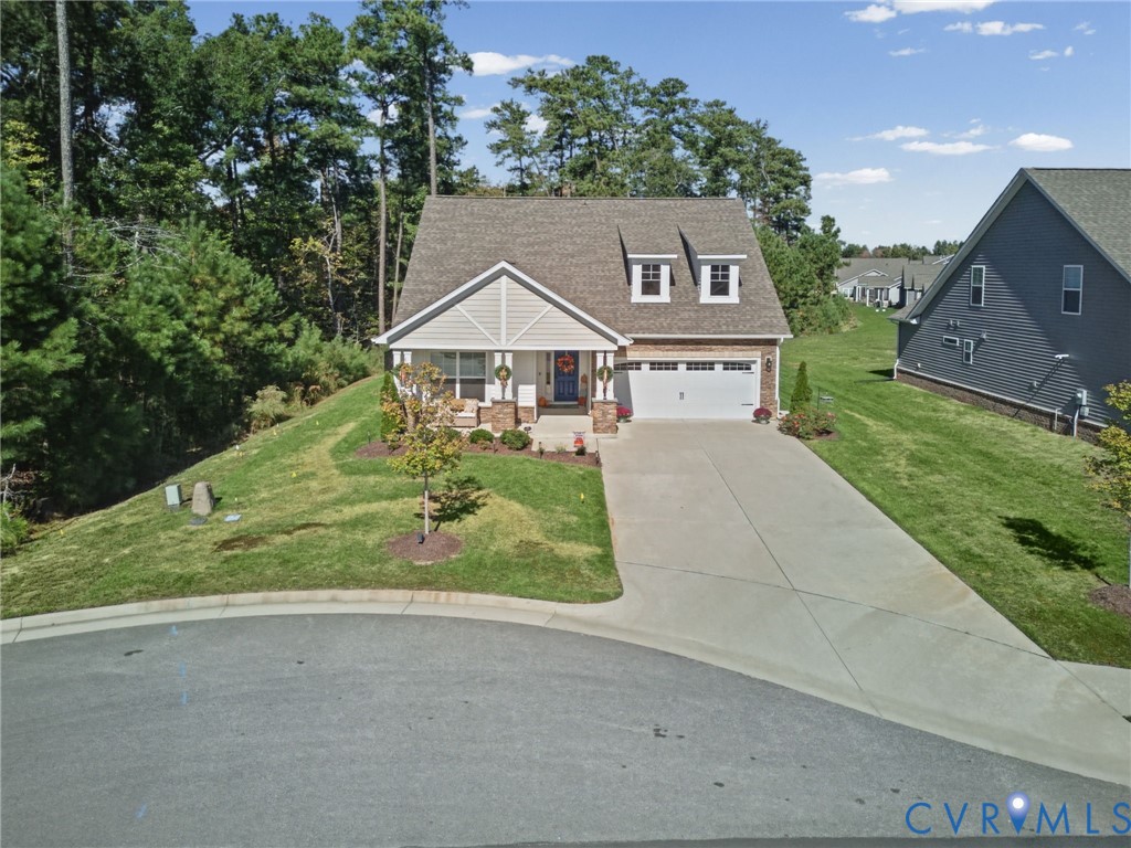 Two-story residence featuring a front-facing attached two-car garage, stone and shingle exterior detailing, gabled roofline with dual dormers, and a concrete driveway