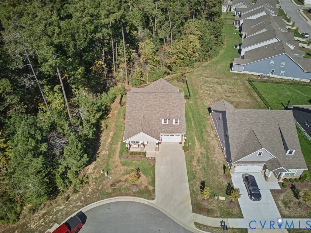 Aerial perspective featuring a multi-gabled roofline, concrete driveway, front covered porch, and rear wooded lot line