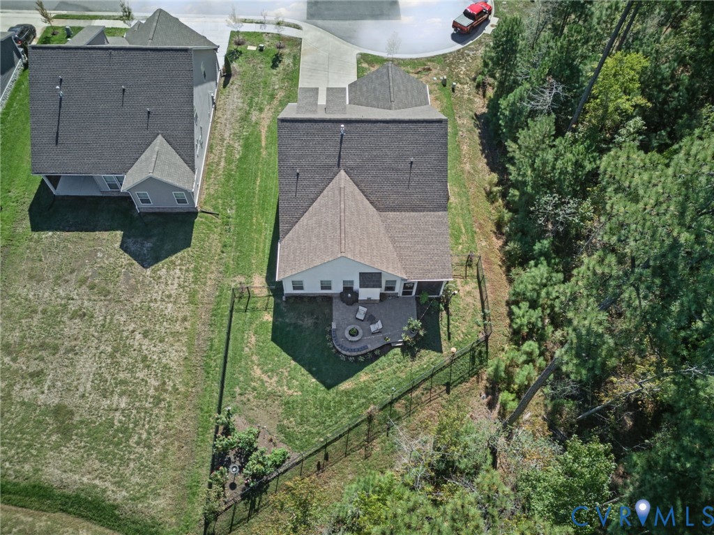 Aerial view of a residential property featuring a fenced backyard, stone-paver patio, and exterior landscaping backing onto wooded acreage