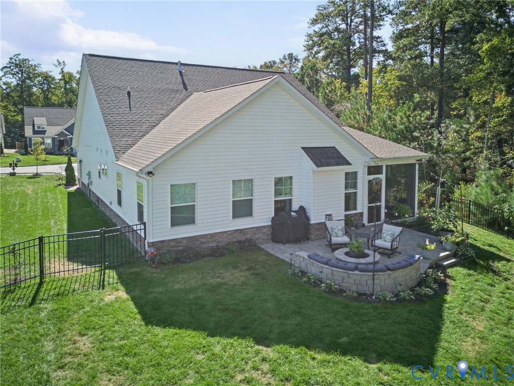 Rear exterior featuring horizontal siding, a stone veneer foundation, a screened porch, a paved patio with a built-in stone fire pit, and a black metal perimeter fence