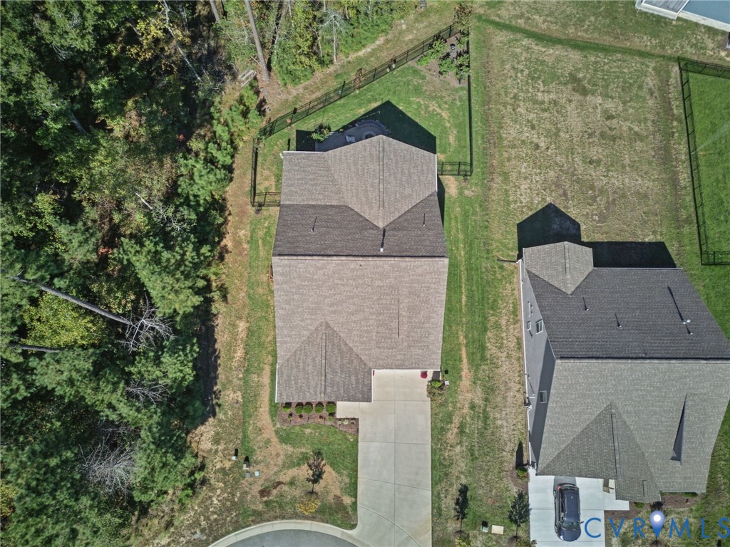 Aerial perspective featuring a multi-gabled roofline, concrete driveway, and a fenced backyard bordered by wooded terrain