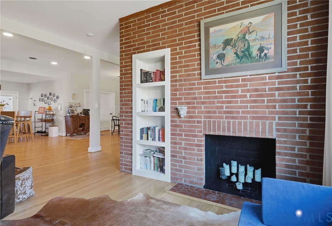 Floor-to-ceiling red brick fireplace featuring a recessed built-in shelving unit, black firebox, and stone hearth, complemented by wood-finish flooring