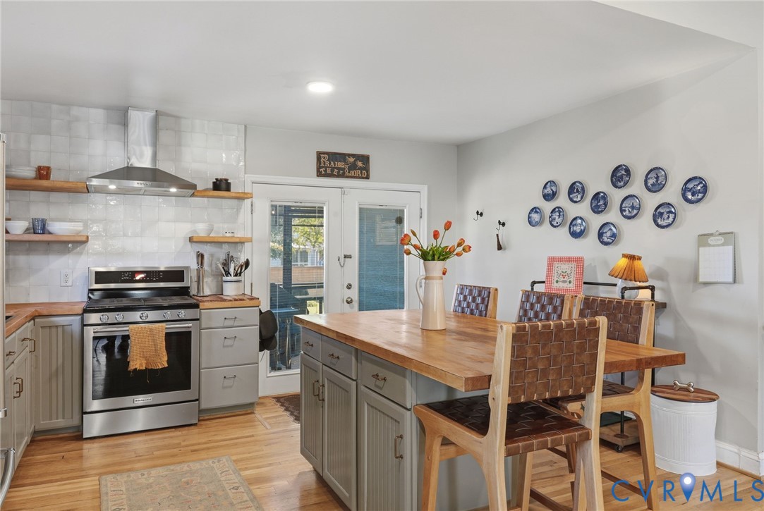 Kitchen featuring stainless steel range, custom wood shelving, center island with wood countertop, and wood-finish flooring