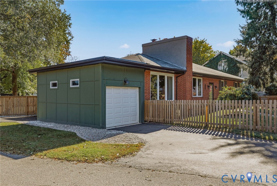 Exterior featuring red brick masonry, green panel siding, a single-car garage, and a wood picket fence