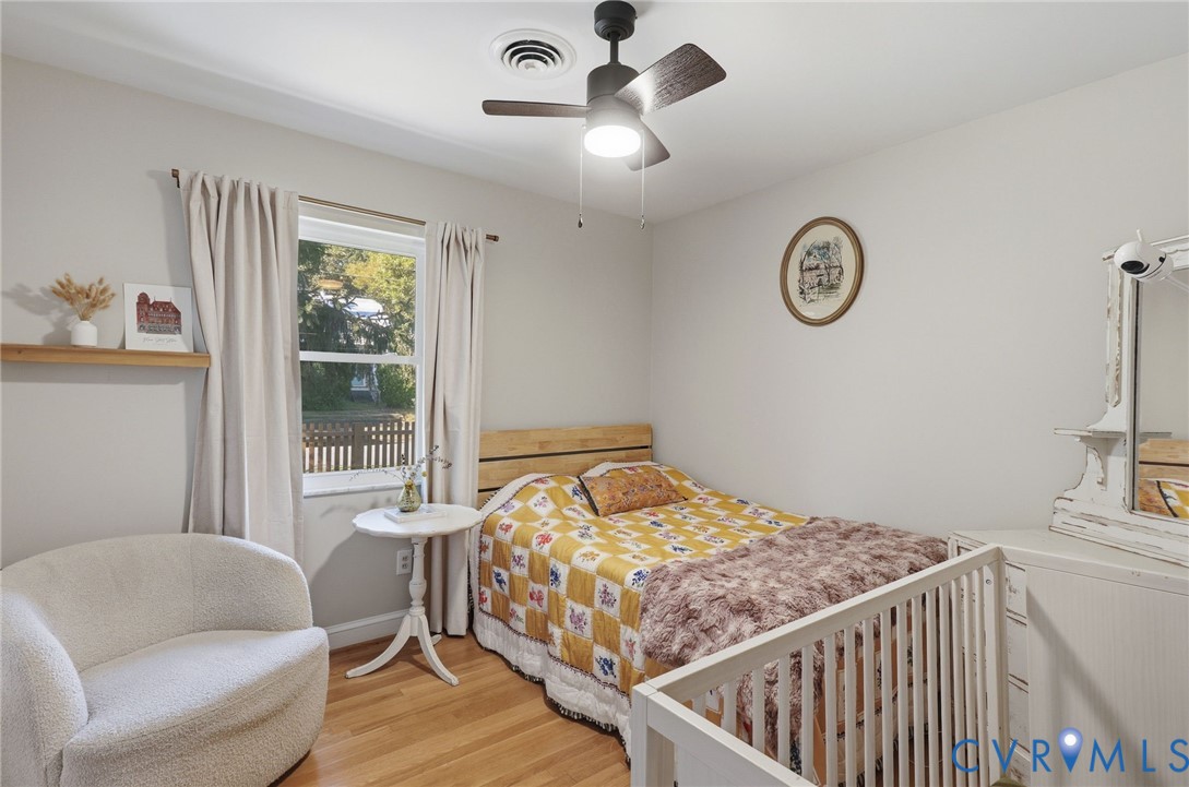 Room featuring wood-finish flooring, a wall-mounted floating shelf, and a ceiling fan with integrated lighting