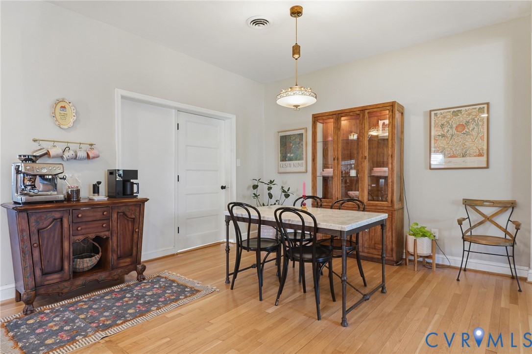 Dining area featuring wood-finish flooring, a tiered metal pendant light fixture, and a white five-panel interior door