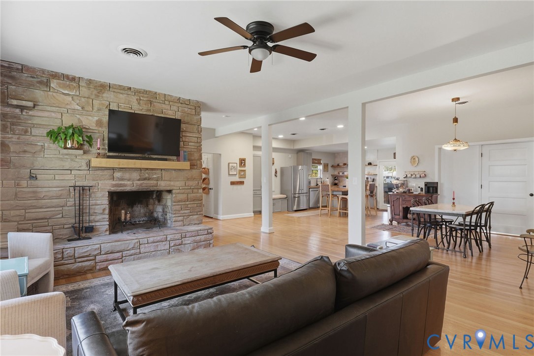 Floor-to-ceiling stone fireplace with a natural wood mantel, wood-finish flooring, recessed lighting, and a ceiling fan