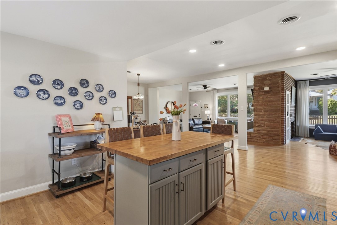 Kitchen island with beadboard cabinetry and a wood countertop, wood-finish flooring, and exposed brick masonry chimney