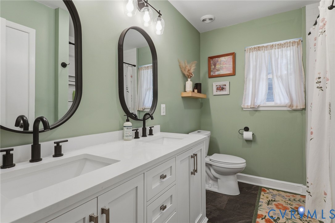 Dual-sink vanity with white cabinetry, solid surface countertop, matte black fixtures, oval mirrors, and integrated overhead lighting