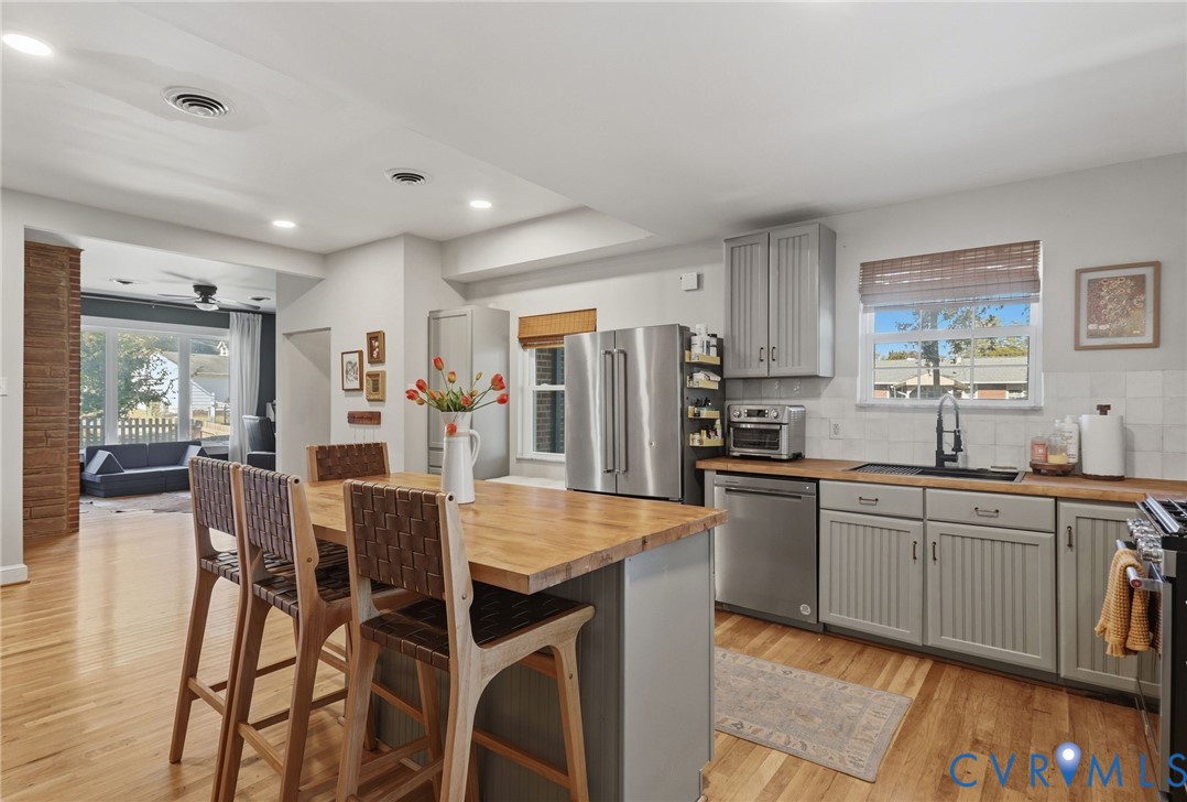 Kitchen featuring wood-finish flooring, a central island with a wood countertop, grey cabinetry, stainless steel appliances, and a tiled backsplash
