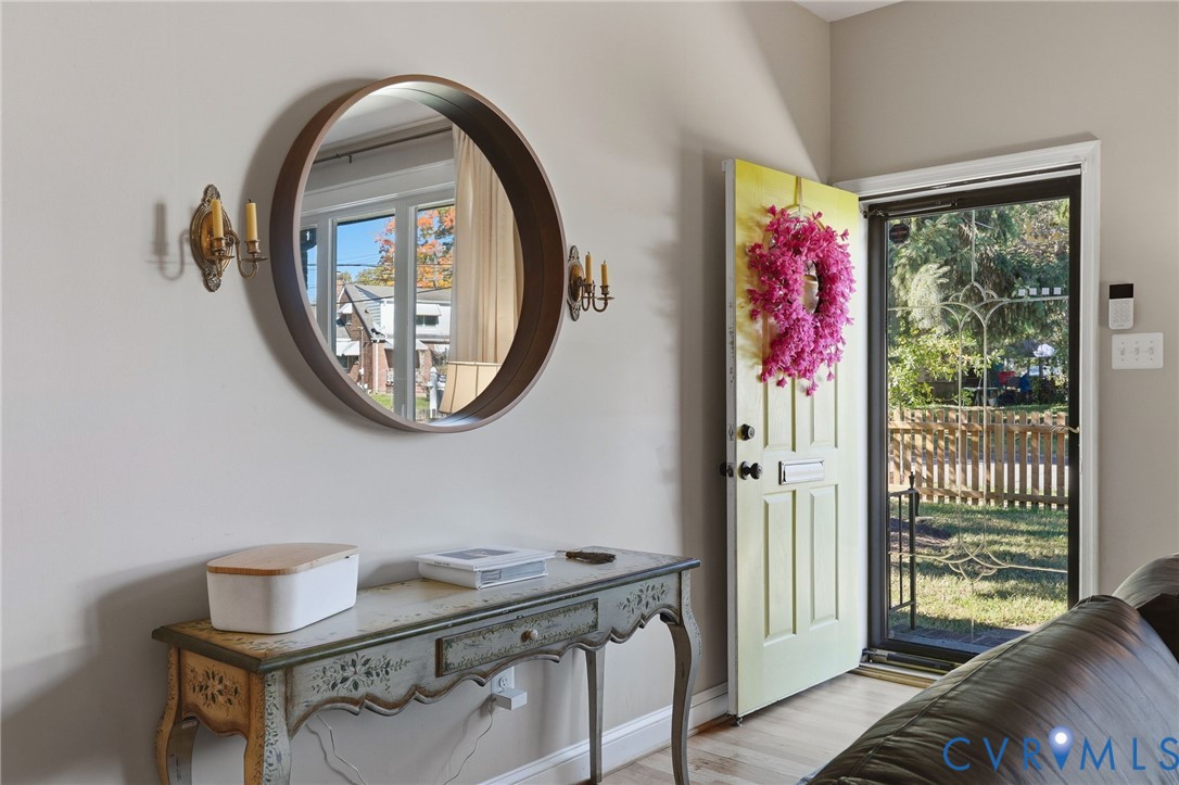 Entryway featuring a solid door with a built-in mail slot, a screen door with decorative metal grillwork, two wall-mounted metallic candle-style sconces, and wood-finish flooring