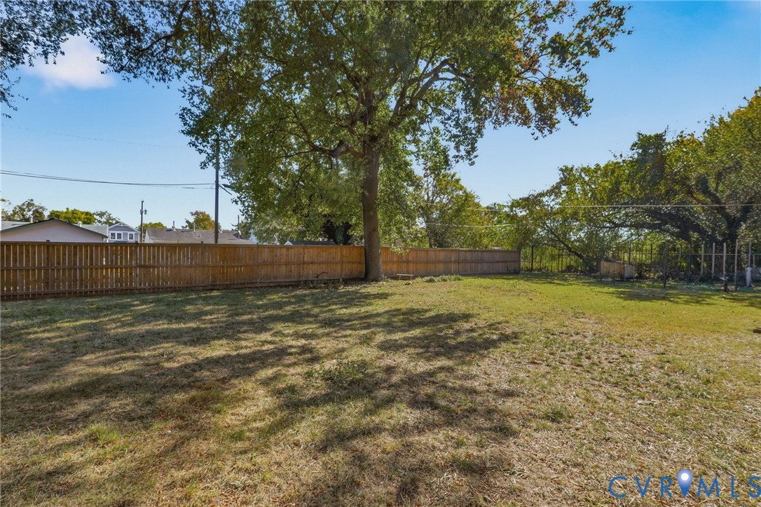 Expansive backyard featuring a wood-panel fence, open lawn space, and mature trees